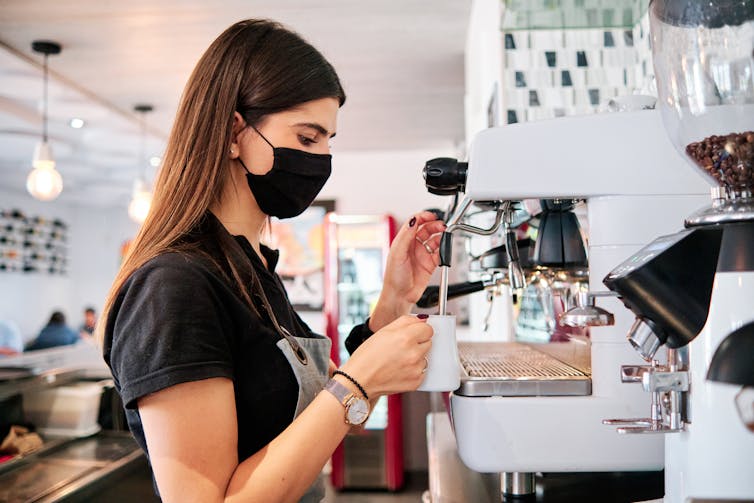 Barista with mask making coffee.
