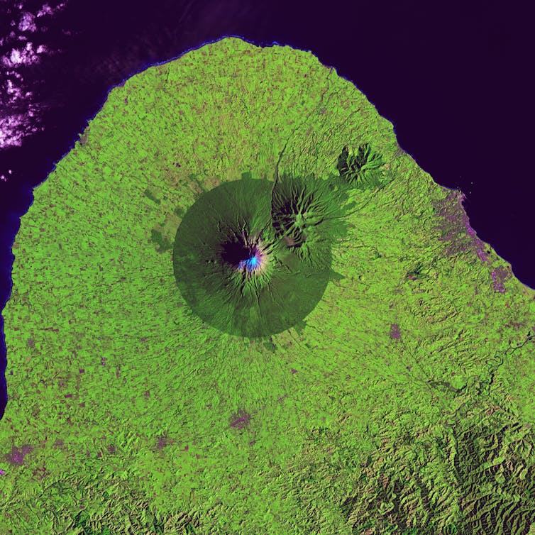 Volcano crater from above surrounded by a dark green circle of forest