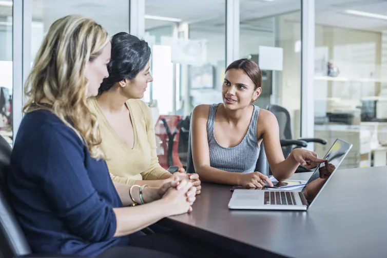 A First Nations person sits with two people and a laptop.