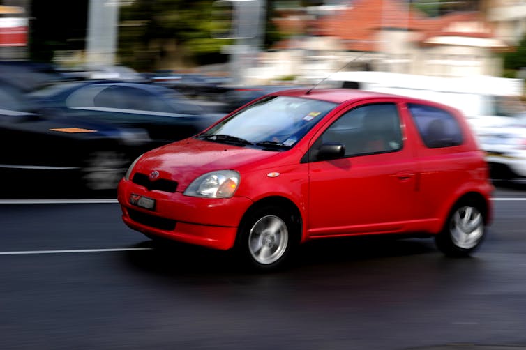 red car drives on city street