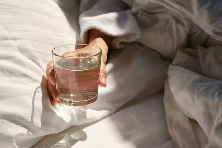 Tangan memegang segelas air di tempat tidur
