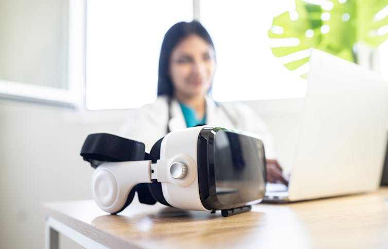 A VR headset sits on a desk in front of a doctor.