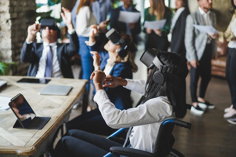 A group of professionals in an office wearing VR headsets and interacting in the metaverse, focus is on a young woman in a wheelchair