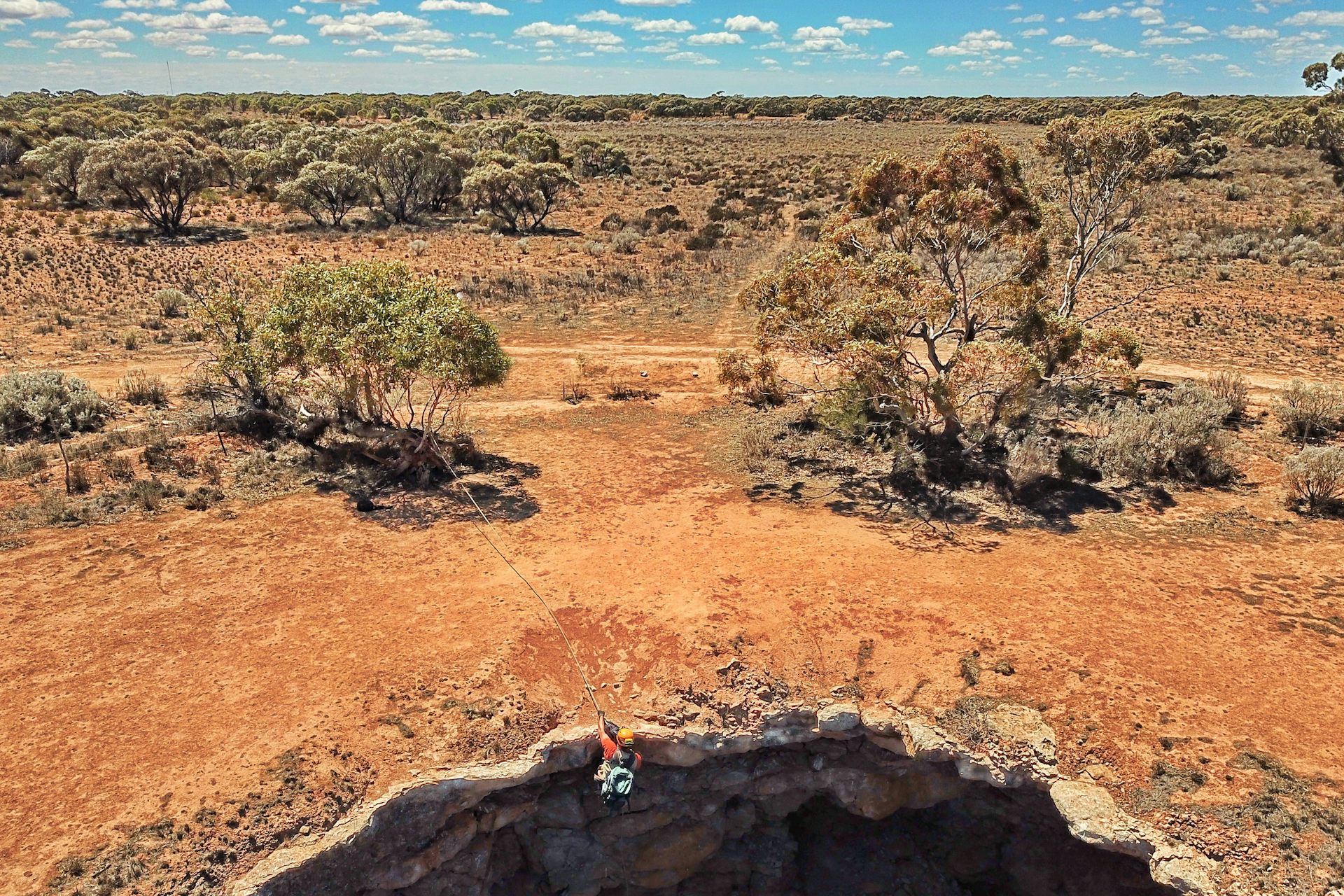 Man abseils into a cave opening in a flat plain