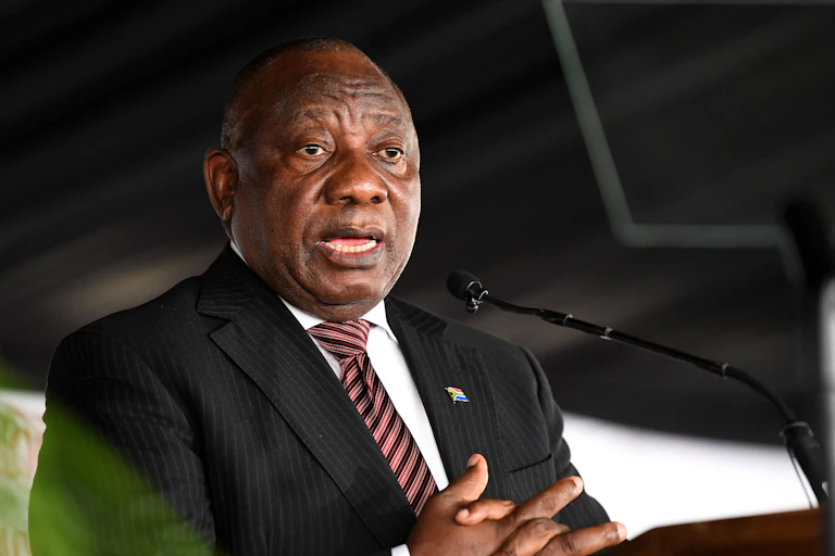 A man wearing a suit and tie clutches his hands as he speaks into a small microphone at a podium.