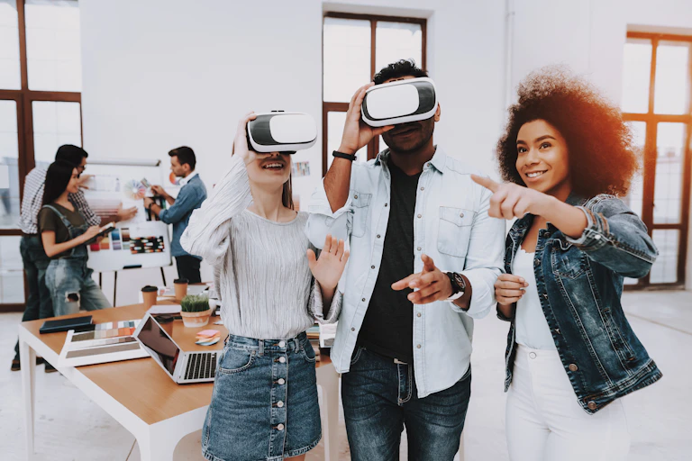 Two students peer into virtual reality devices as a third student stands nearby.