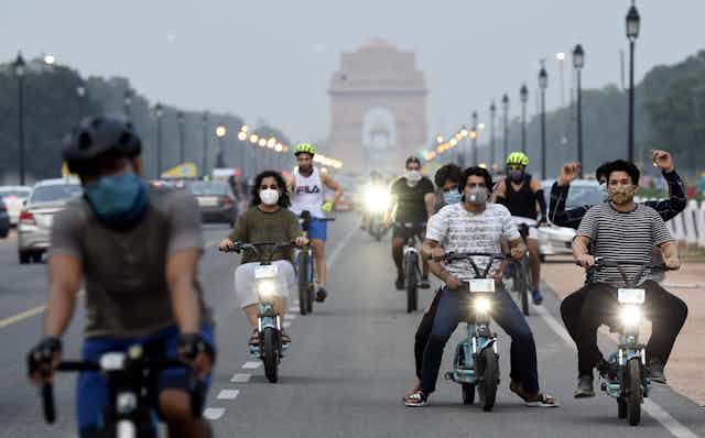 Young people ride bicycles and electric scooters on the bike lanes of a busy road in New Delhi.