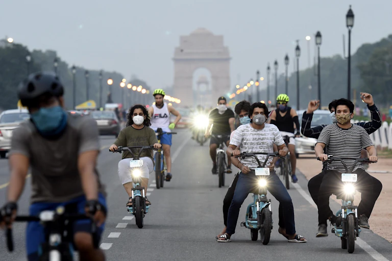 Young people ride bicycles and electric scooters on the bike lanes of a busy road in New Delhi.