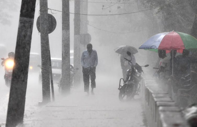 People walk in a heavy downpour. One man is drenched, and even umbrellas don't seem to be helping.