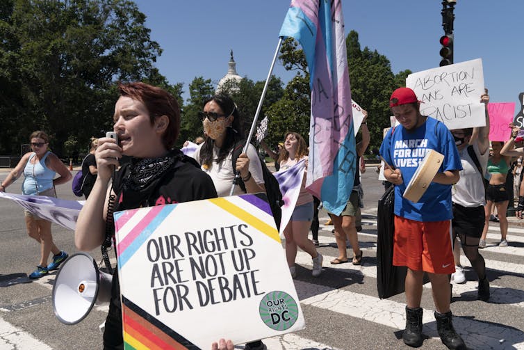 A woman protester carries a sign that reads Our Rights Are Not Up For Debate