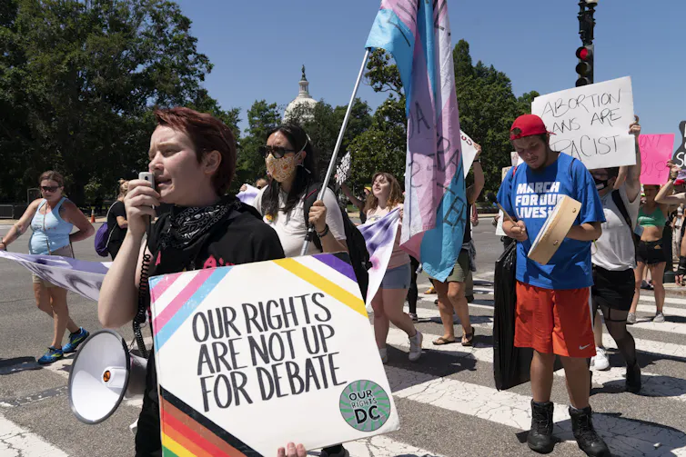 A woman protester carries a sign that reads Our Rights Are Not Up For Debate