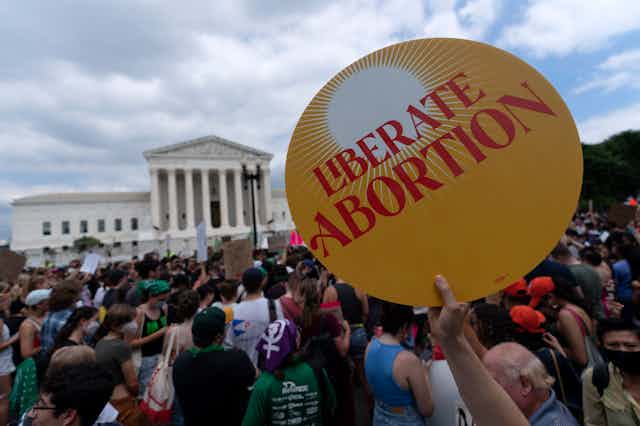 An person holds a sign that reads Liberate Abortion with the U.S. Supreme Court in the background.