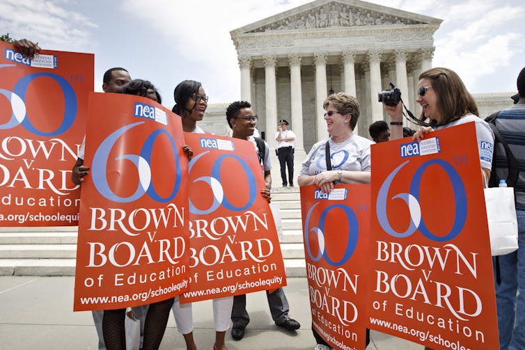 People stand in front of a court building holding banners that pay tribute to the 60th anniversary of a landmark court decision.