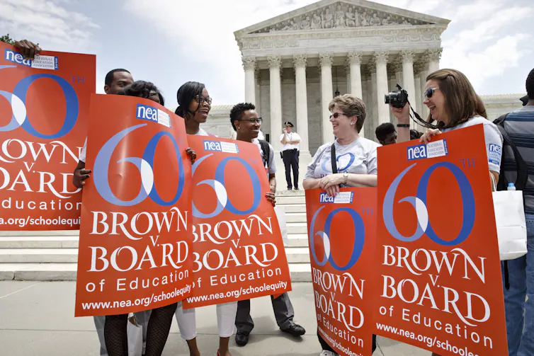 People stand in front of a court building holding banners that pay tribute to the 60th anniversary of a landmark court decision.