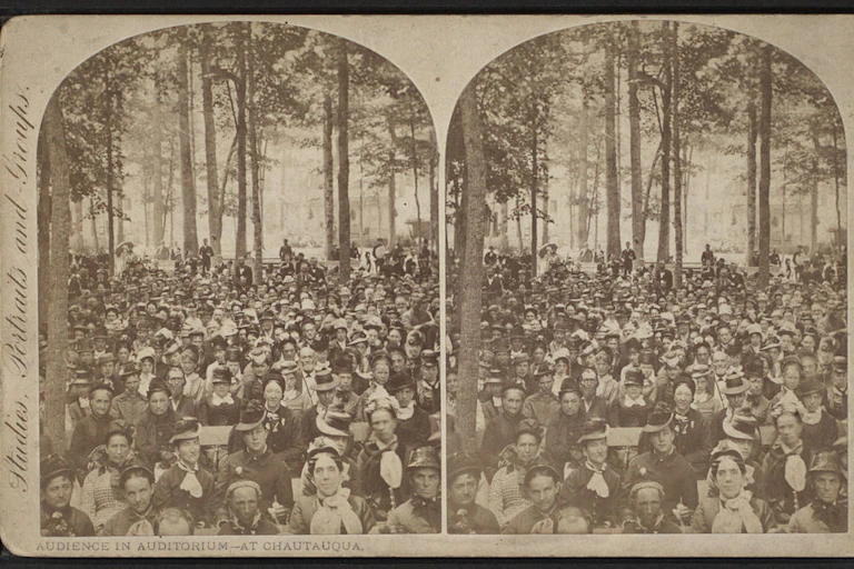 A black and white postcard shows two copies of a photograph of a large crowd seated among trees.