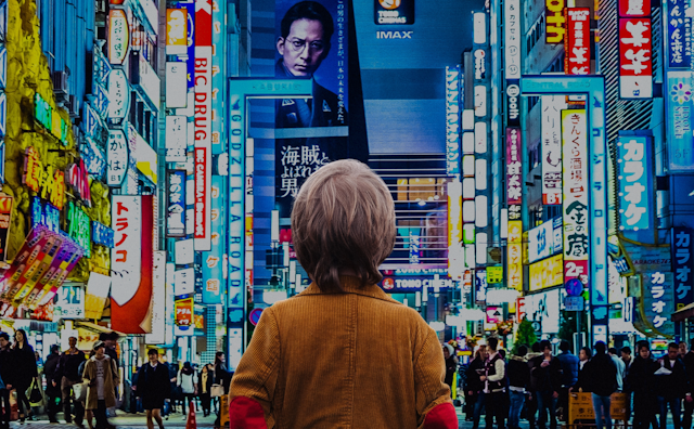 A child standing facing a busy Tokyo street, covered in screens.