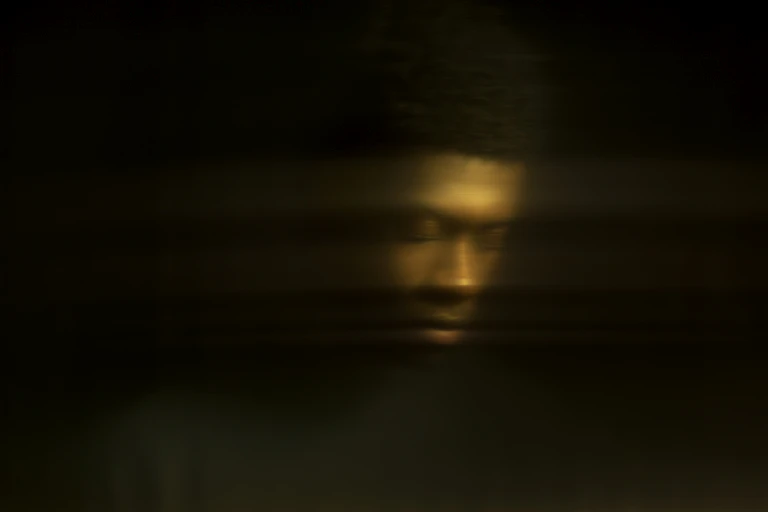 a dark background and a man's face, blurry, looking down