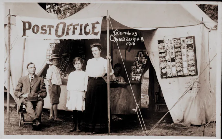 A black and white photo shows two children and two adults outside a post office in a tent.