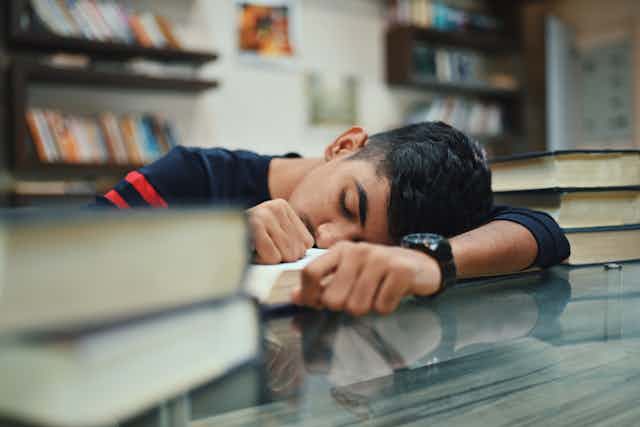 Teen boy sleeping in a school library with his head resting on the table.