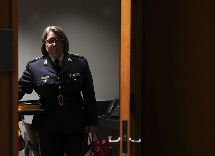 A woman wears an RCMP uniform, stands in a doorway