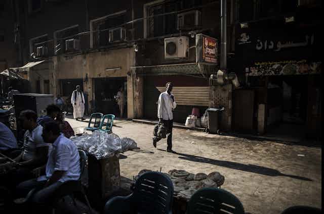 A man walks down a street with a Sudanese flags and men sitting at tables