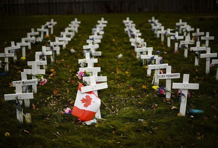White crosses in a grassy patch, with a Canadian flag fastened to one.