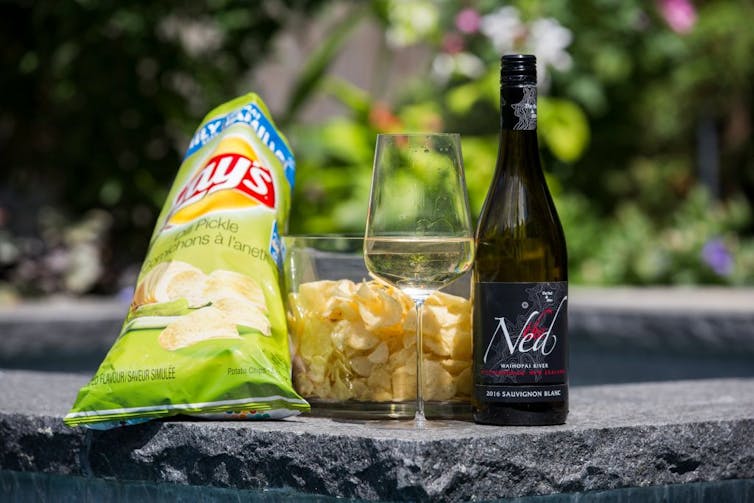 Green bag of potato chips next to bowl of chips and bottle of wine.