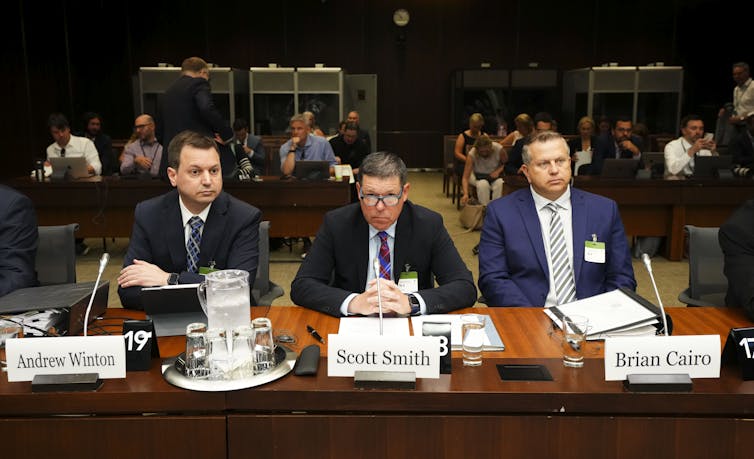 Three men is suits sit behind a table.
