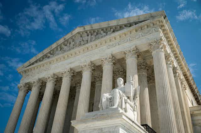 A view of the front of the US Supreme Court building with columns and a statue of a seated person.