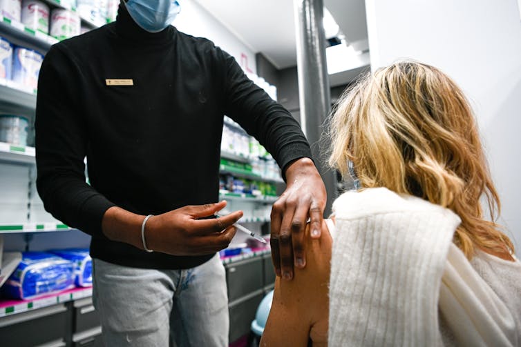 Pharmacist giving vaccine in upper arm of seated female customer