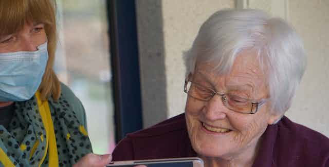 An aged care worker holds a smartphone up to an elderly resident.