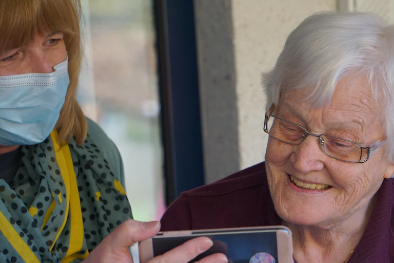 An aged care worker holds a smartphone up to an elderly resident.
