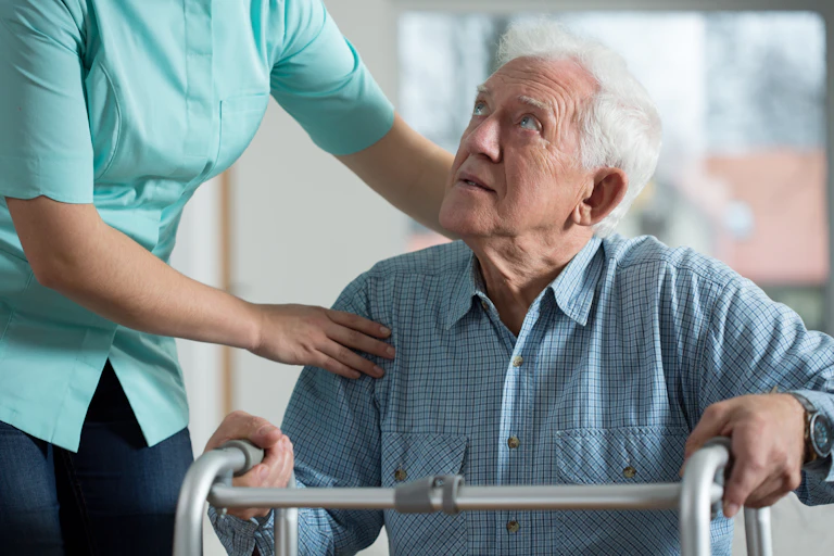worker helps older man with walking frame
