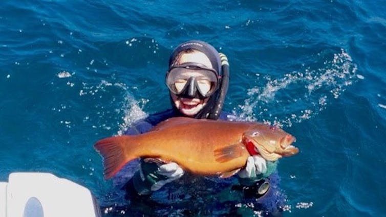 Man snorkeling in the ocean, holding up a large orange fish