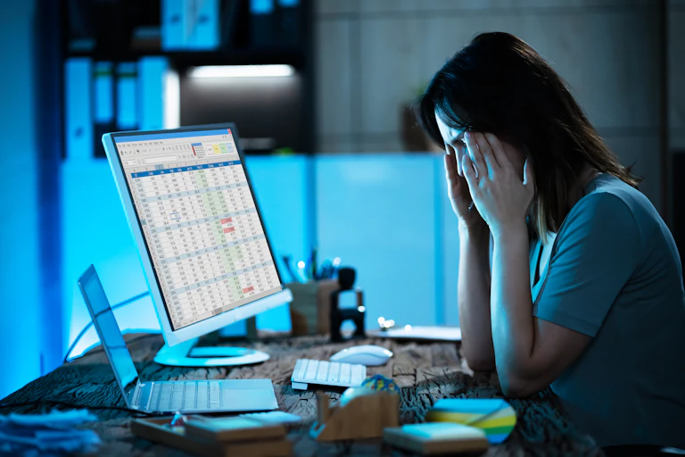 Woman looking at spreadsheet on computer massages her temples.