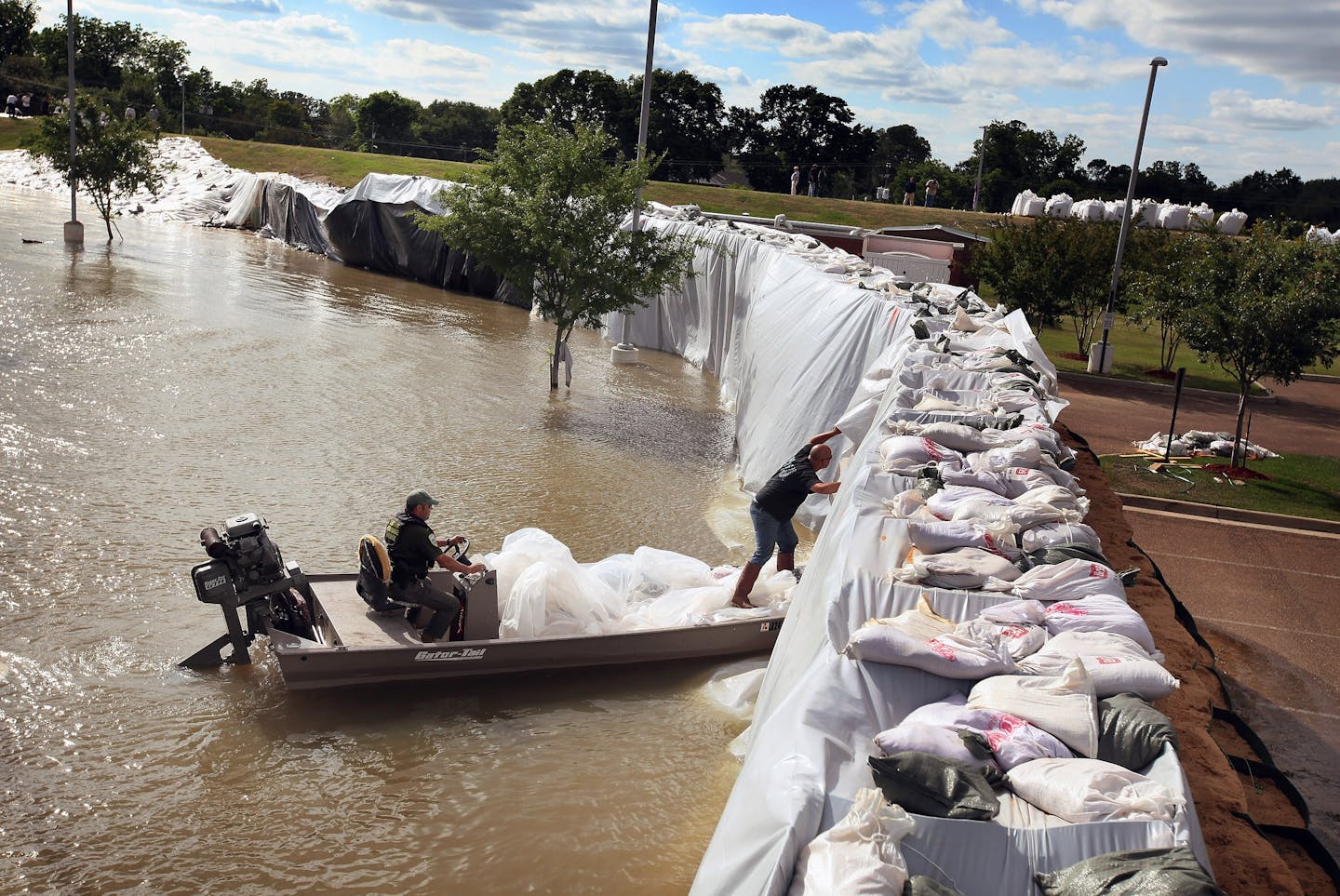 A man in a boat peers under sheeting along a level. The river side is higher than the dry side across the levee.