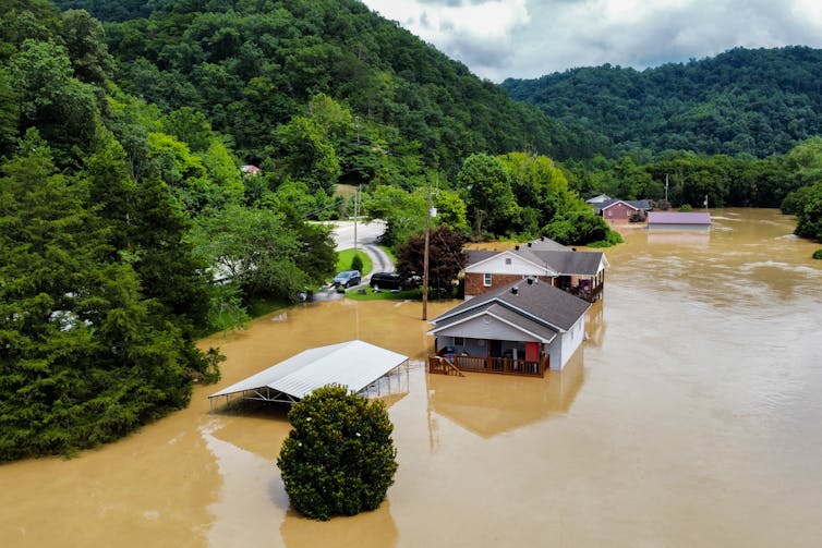 Houses in a steep valley are flooded to their rooflines with muddy water.