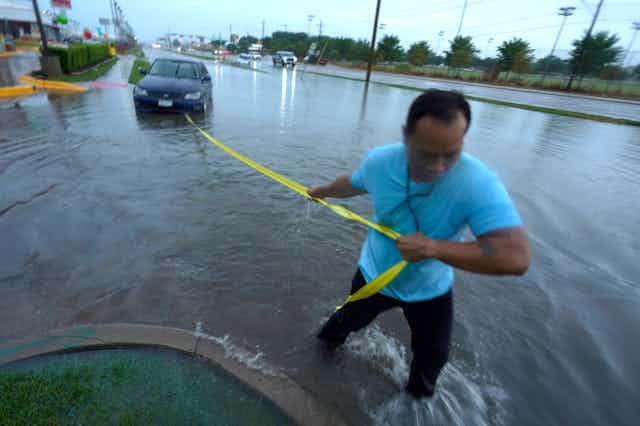 A man holding a strap to car in a flooded roadway to tow it.