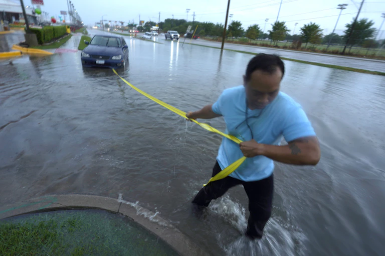 A man holding a strap to car in a flooded roadway to tow it.