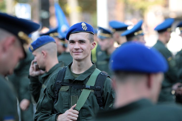 Soldiers in blue berets and green uniforms gather at an anniversary march.
