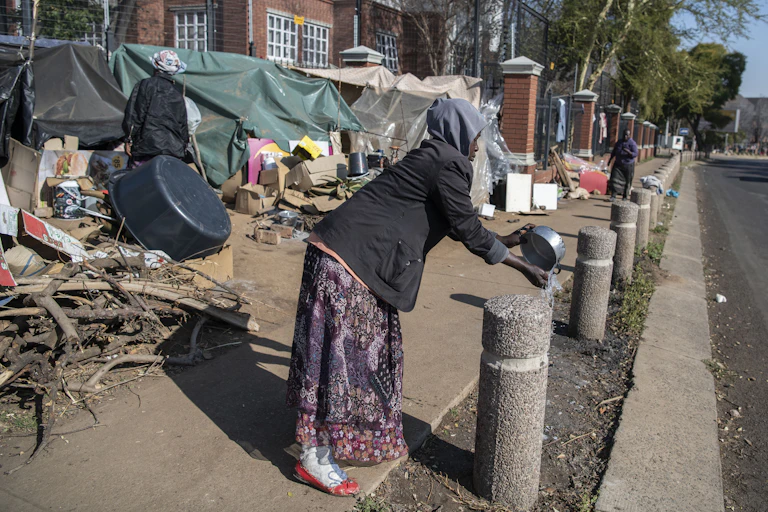a woman washing her hands in front of make-shift shelter