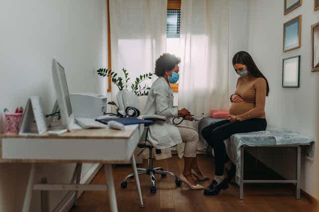 femme enceinte dans un bureau de médecin qui porte un masque
