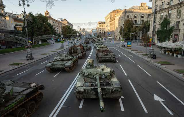 A line of destroyed military vehicles along a city street.