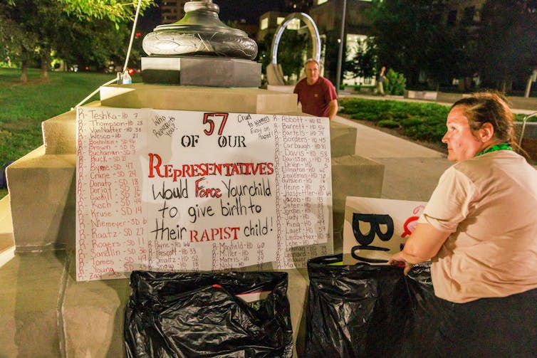 A sign propped up on a fountain outside that lists the names of the 57 Indiana House members who voted to ban abortion.