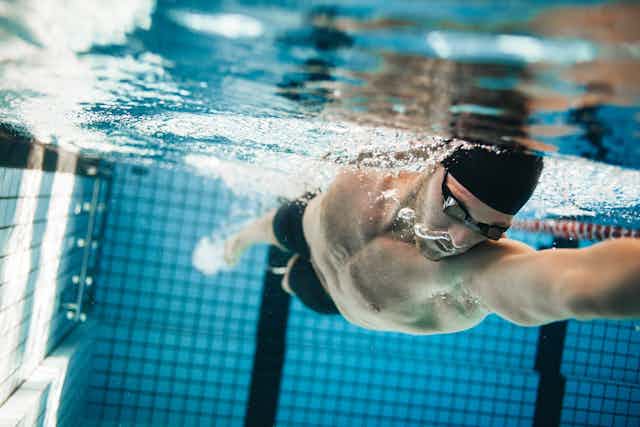 A male swimmer does the breast stoke in the pool. He's wearing goggles and a swim cap