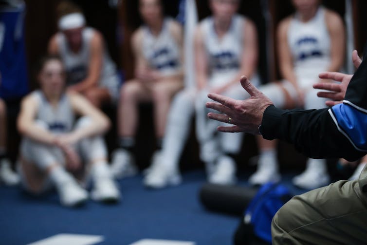 A coach gives a talk in the locker room to a group of athletes.