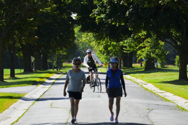 A cyclist and two people make their way down a tree-lined outdoor path