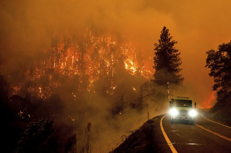A firetruck drives near a burning wildfire.