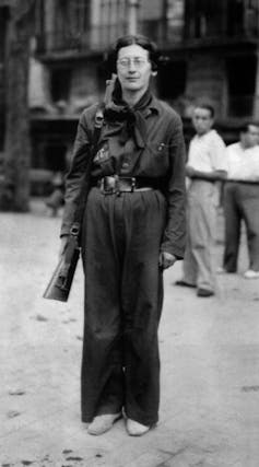 A 1936 photo of French philosopher Simone Weil dressed in military clothing holding a rifle.