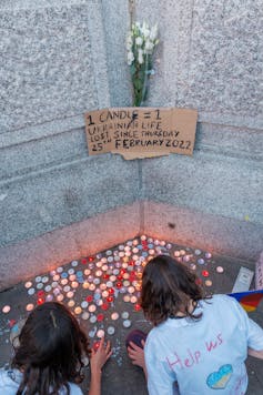 Two young people place candles on the ground.